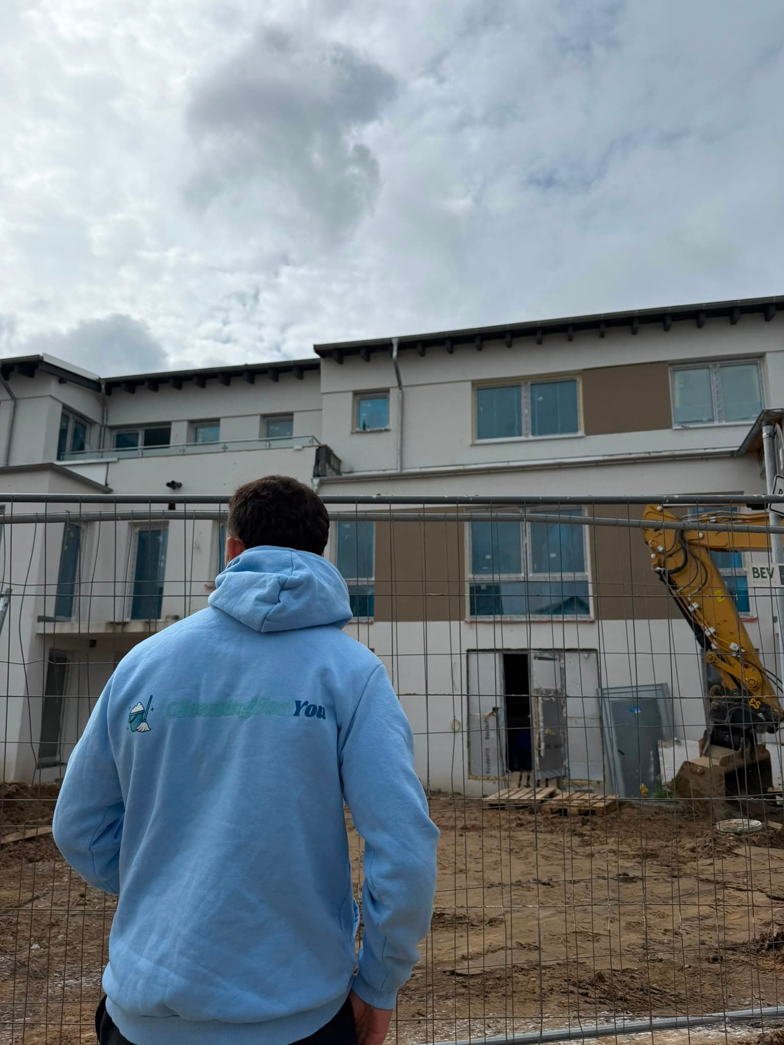 Mitarbeiter von CleaningForYou, Gebäudereinigung aus Neuss, im Firmen-Hoodie vor einem Objekt auf der Baustelle